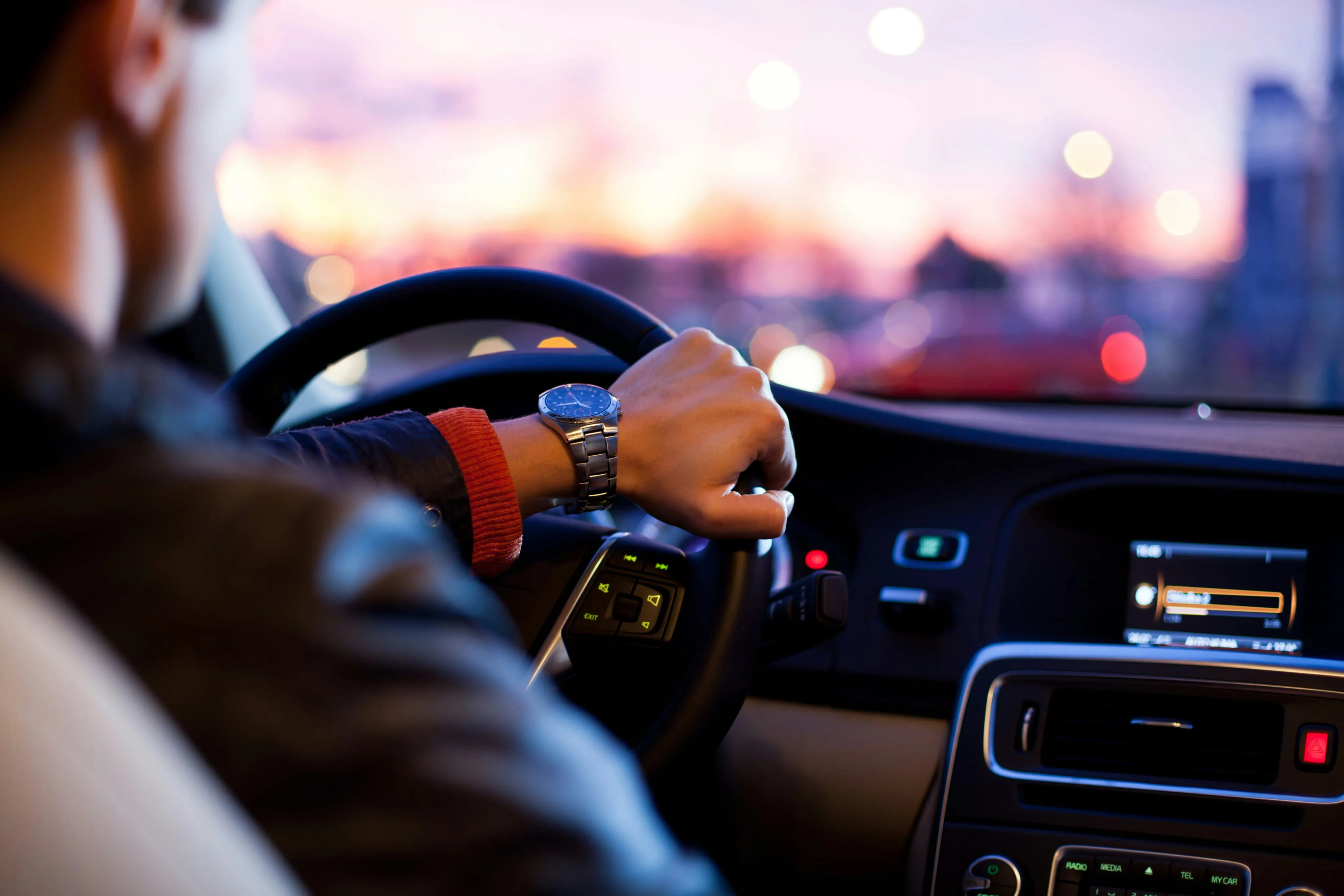 Hands on a steering wheel driving toward a sunset